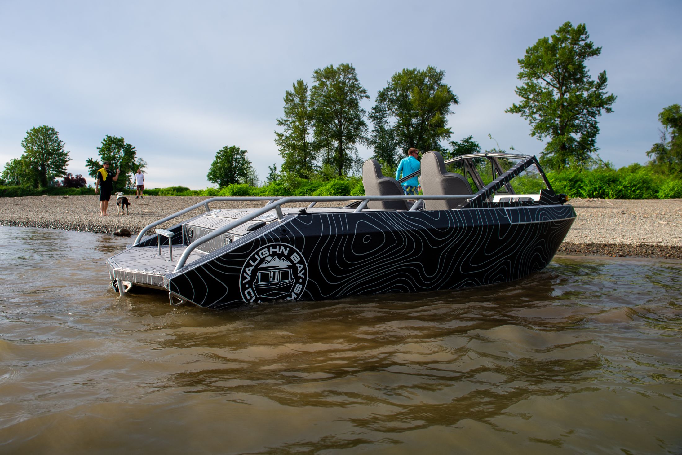A welded aluminum Vaughn Bay Customs jet boat running hard through shallow river water, throwing spray from the pump