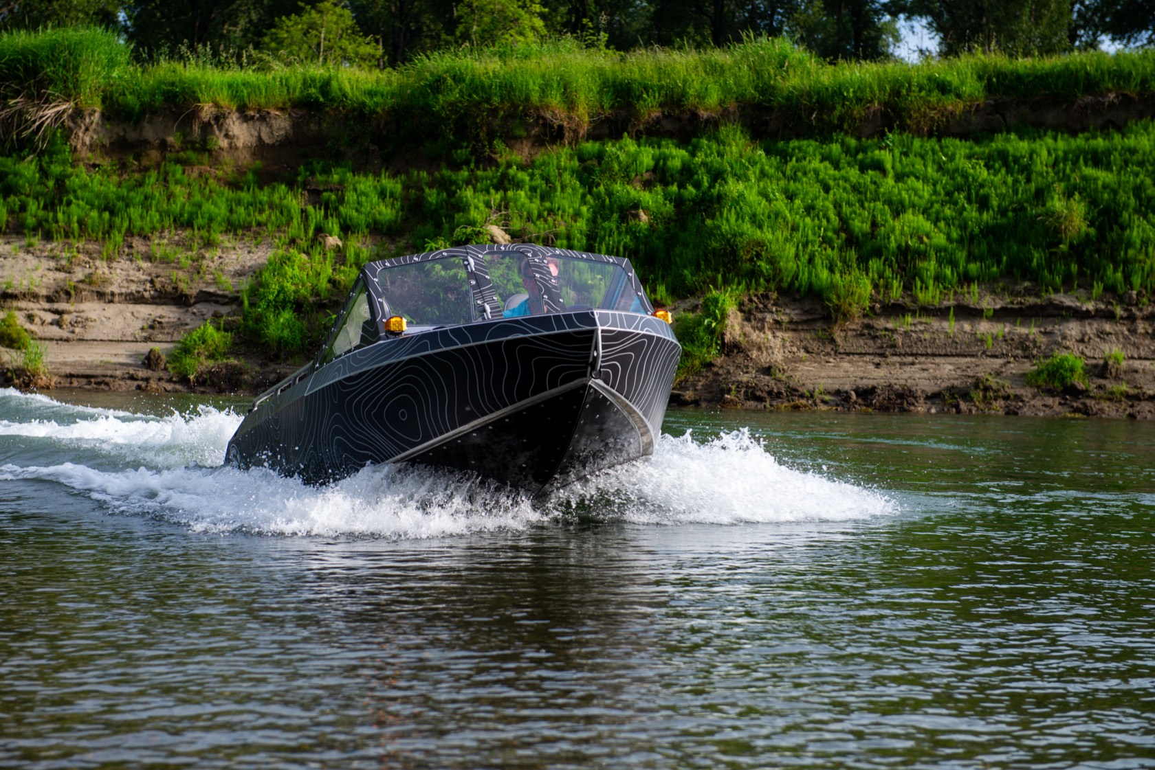 Head-on view of the topo-wrap jet boat running upriver at speed, throwing a bow wake