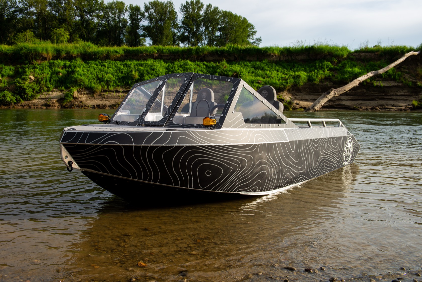Front-quarter view of the topo-wrap jet boat nosed up on a gravel bar under a bright sky