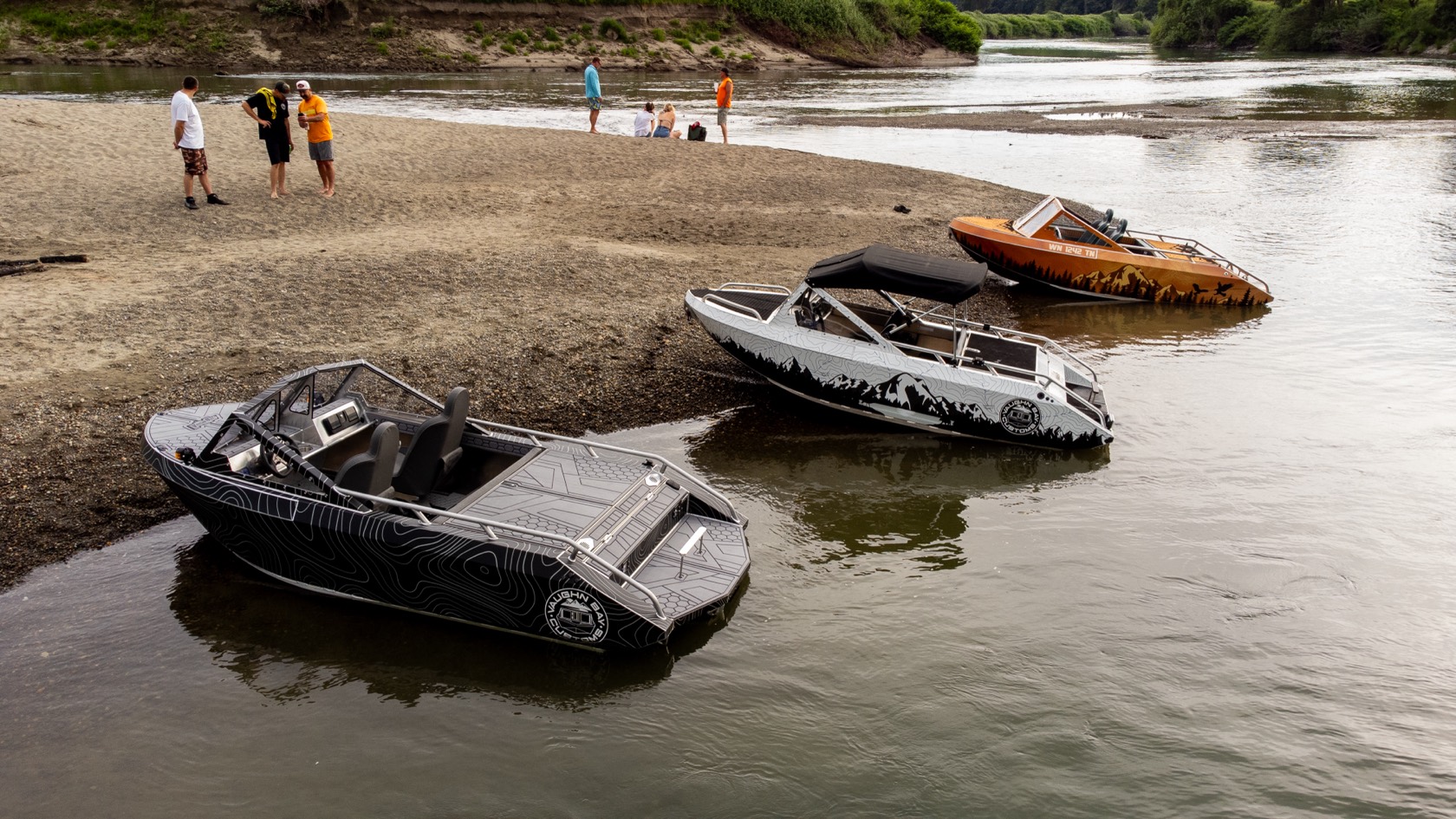 Aerial view of the topo-wrap jet boat beached beside two other Vaughn Bay Customs boats on a river sandbar