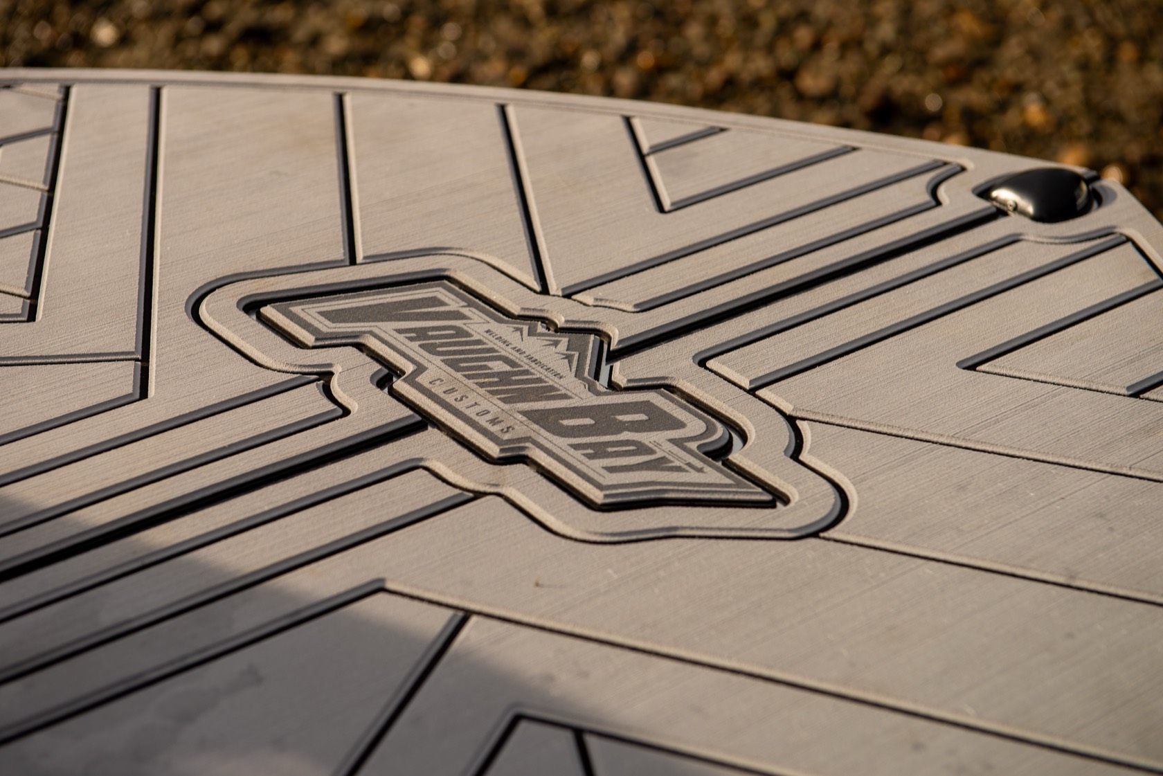 Close-up of the Vaughn Bay Customs logo embossed into the boat's non-skid deck matting, backlit at golden hour