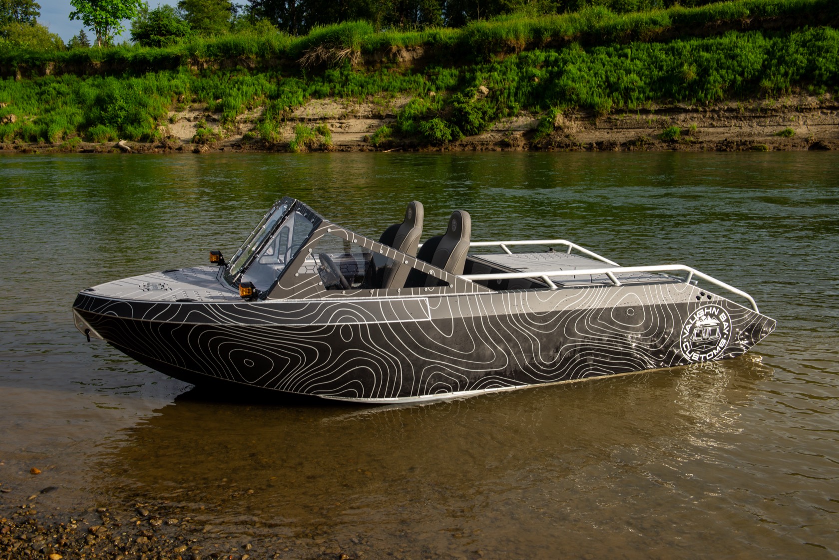 Port-side profile of the black topo-wrap Vaughn Bay Customs jet boat on a river bar in warm afternoon light