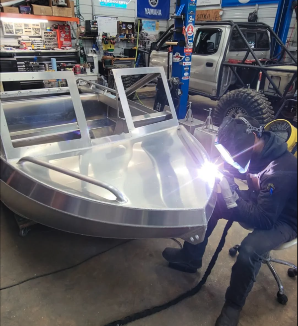 A welder in a hood TIG-welding the aluminum deck of a Vaughn Bay Customs jet boat in the shop