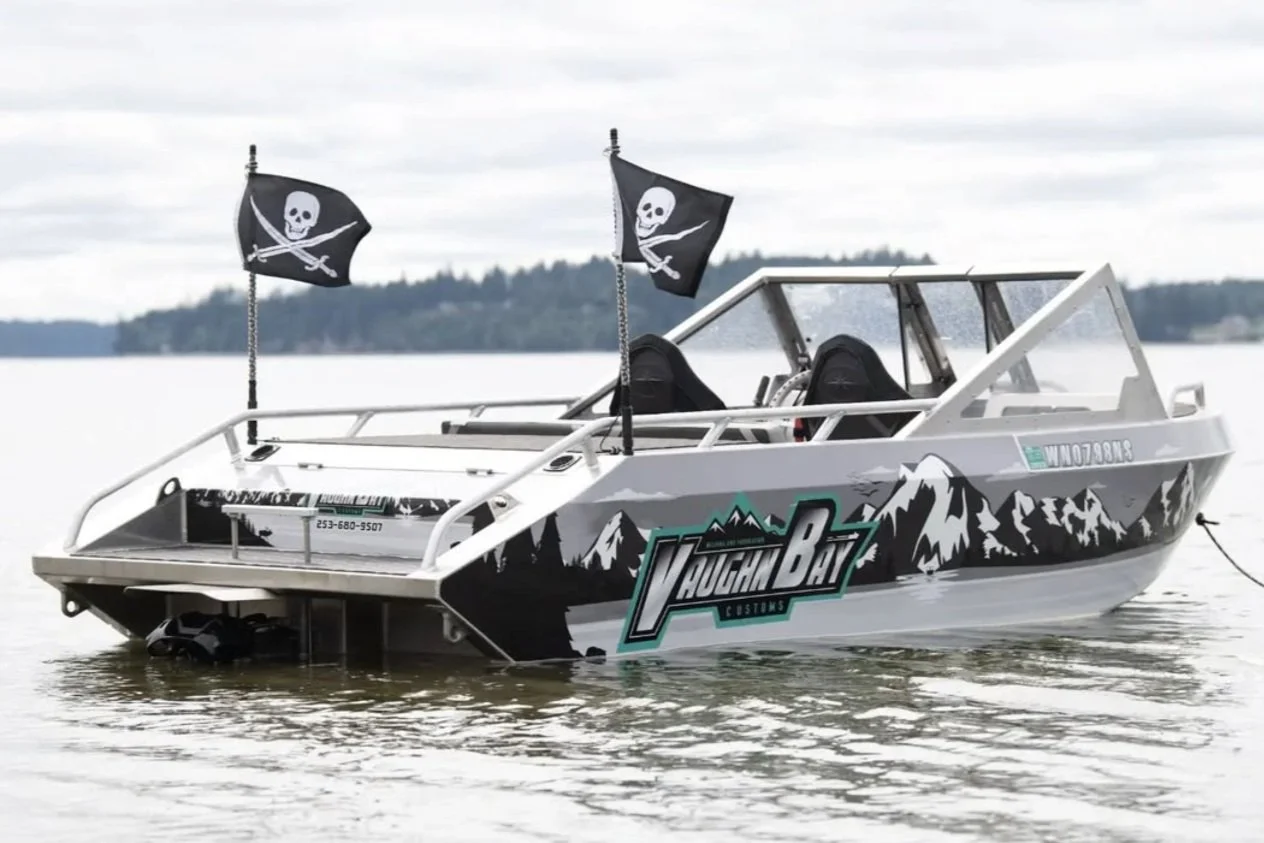 An earlier Vaughn Bay Customs VB12 mini jet boat in a custom mountain-logo wrap with pirate flags, on a calm Washington lake