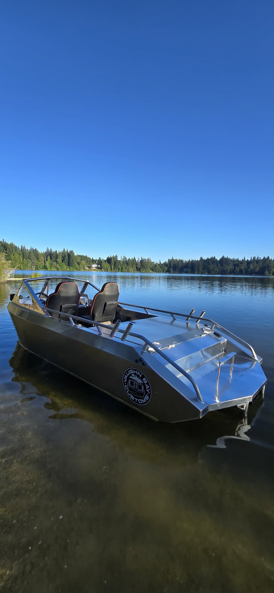Front-quarter view of a finished Vaughn Bay Customs VB14 welded aluminum jet boat floating on a calm forest lake